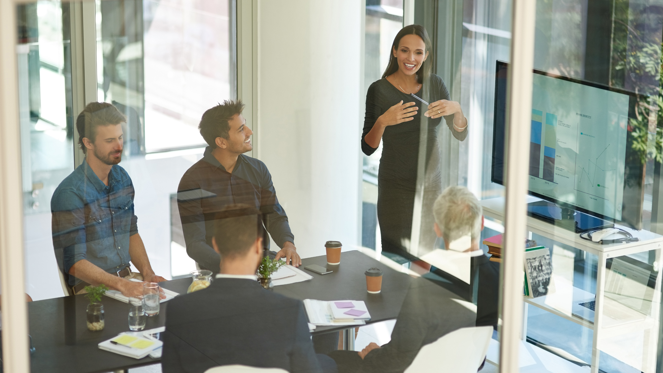  In a meeting room, a woman delivers a presentation on RevOps while a group of attentive individuals listens and takes notes.